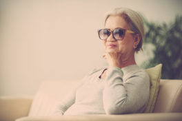 Ältere Frau mit Sonnenbrille sitzt auf dem Sofa