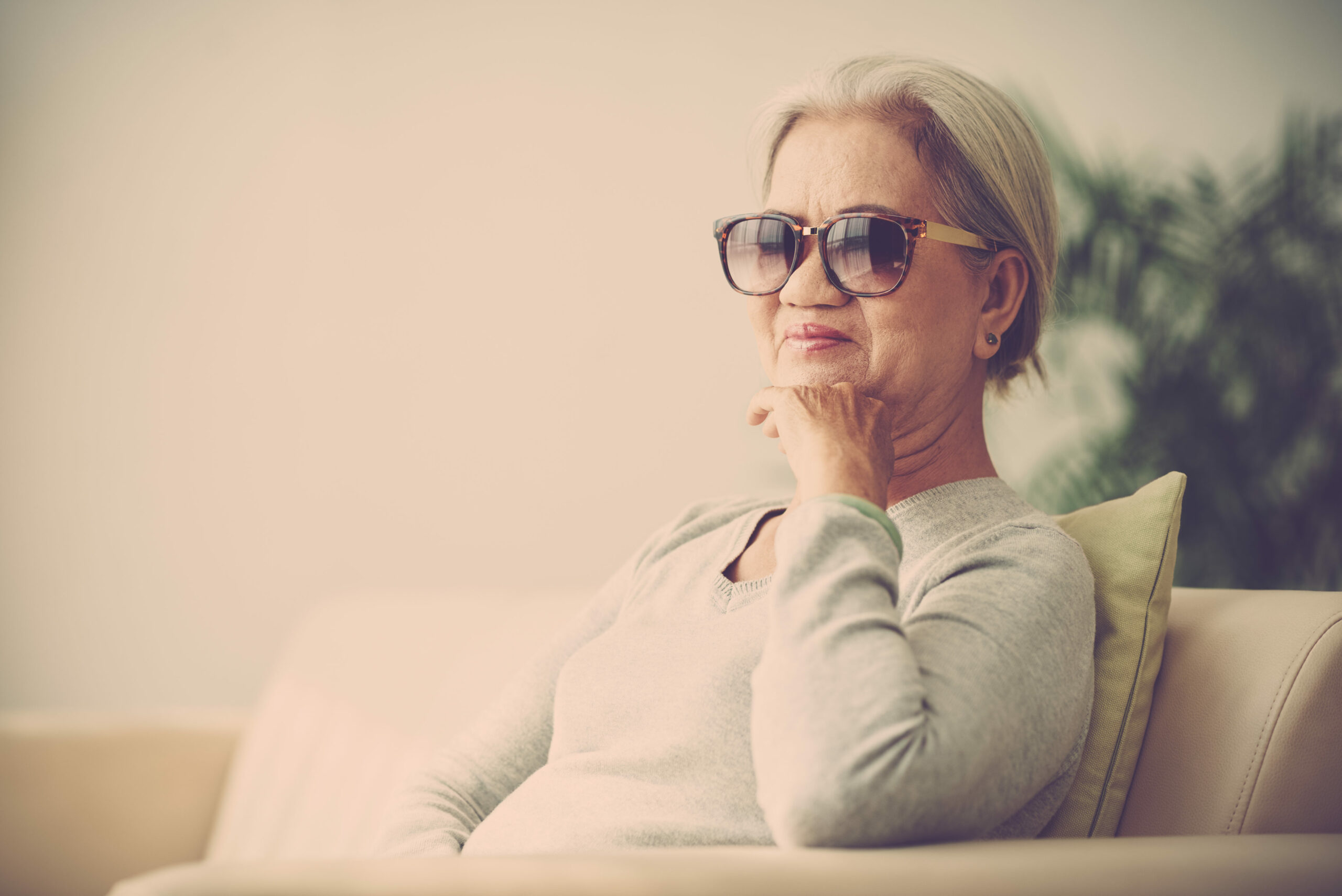 Ältere Frau mit Sonnenbrille sitzt auf dem Sofa