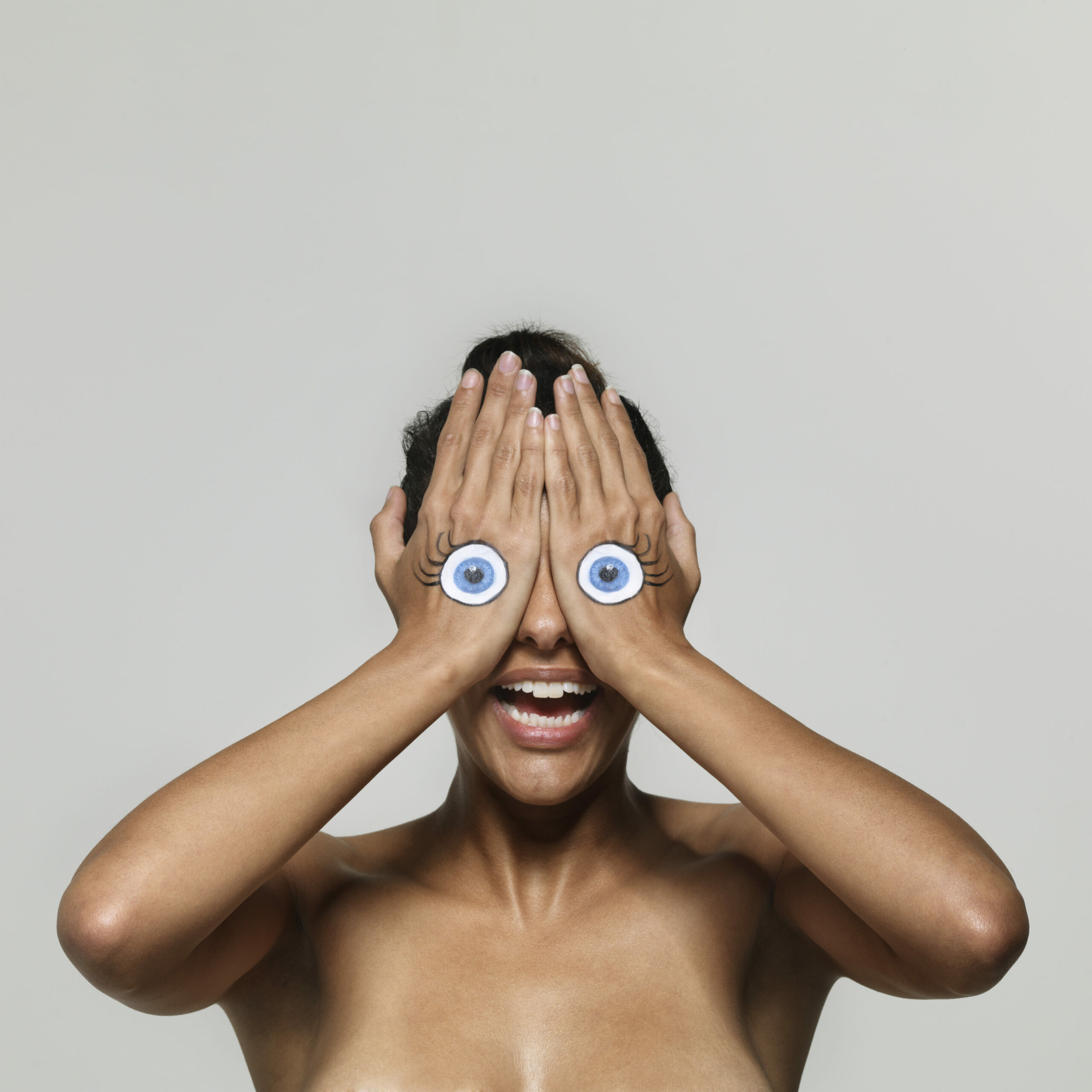 Frau hält Hände mit aufgemalten Augen vor Gesicht - Lidrandpflege