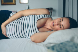 Schwangere Frau im gestreiften Tshirt schläft auf dem Bett.