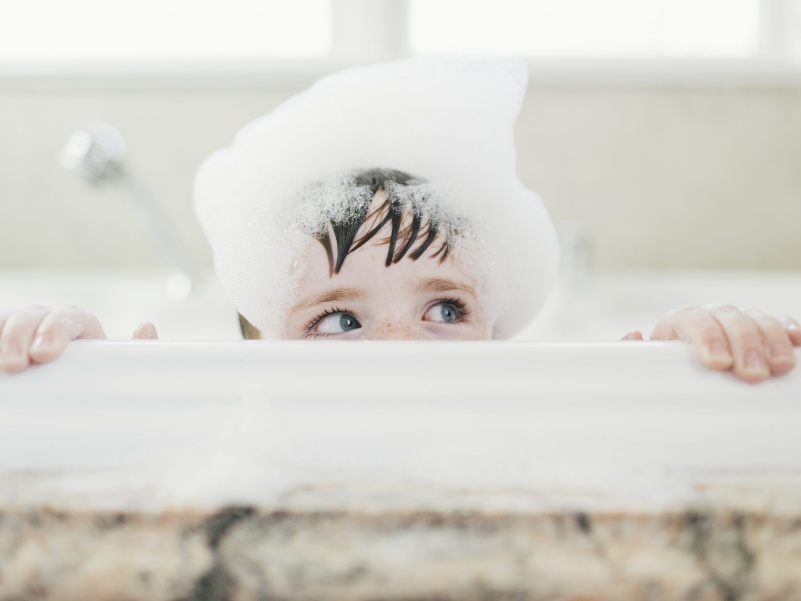 Kontaktallergie Auslöser: Kind mit Schaum auf dem Kopf schaut über Badewannenrand