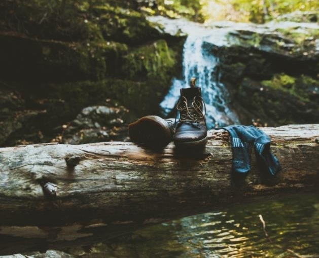 Gesunde Füsse: Wanderstiefel und Socken liegen auf einem Baumstamm quer über einem Bach.