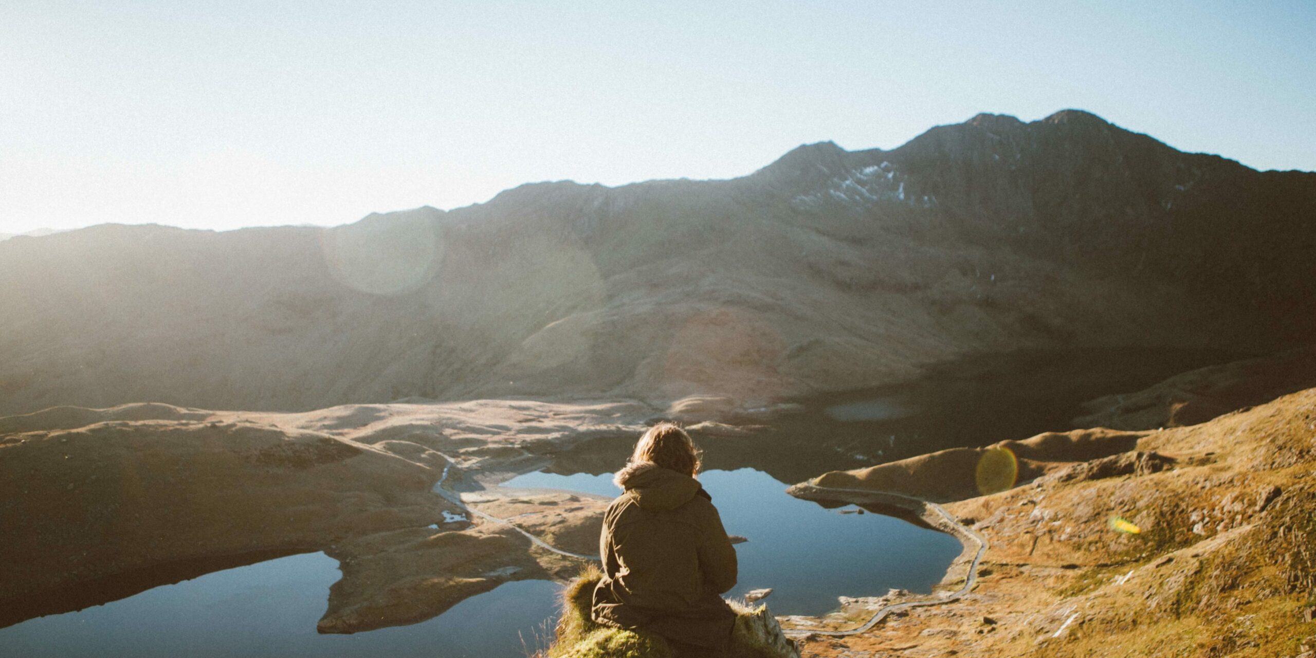 Eine Frau sitzt auf einem Felsen und schaut auf einen Fluss, der sich zwischen den Bergen durchschlängelt und Adventskalendertürchen 10.