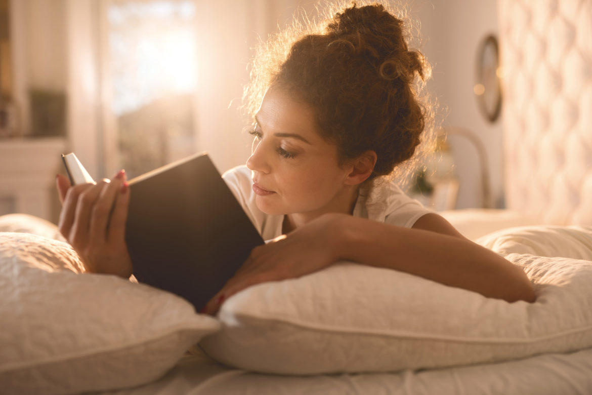 Entspannte Frau liegt im Bett und liest ein Buch