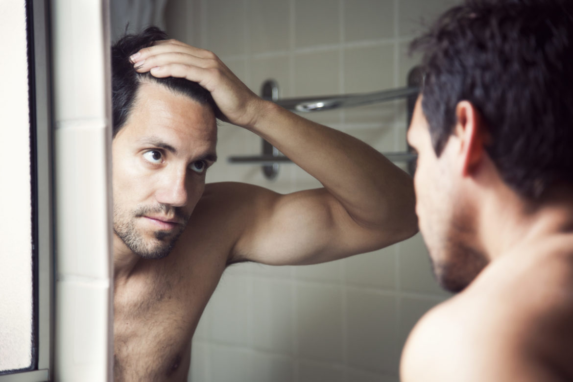 Mann schaut seine Haare an im Spiegel