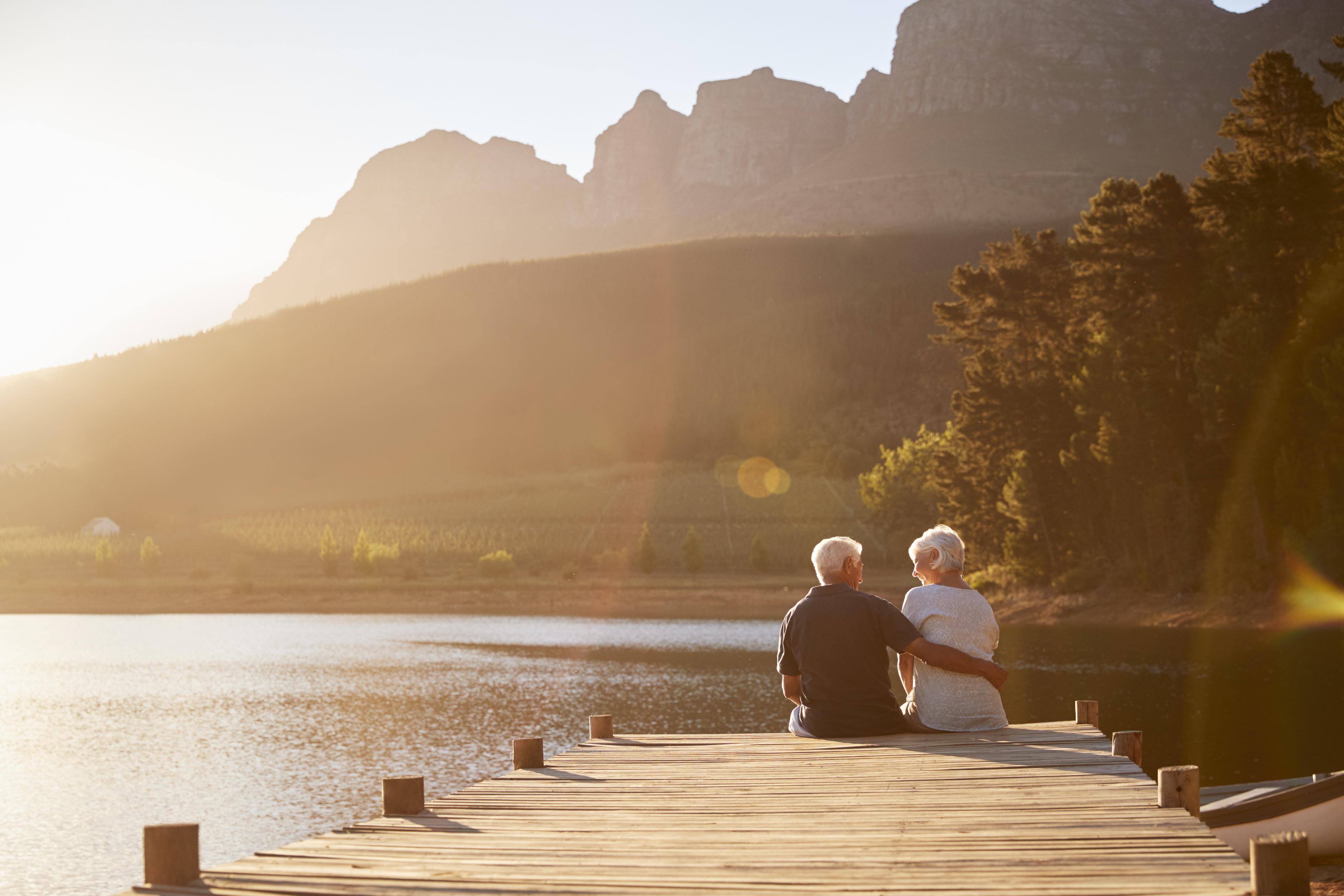 Ein älteres Paar sitzt gemeinsam auf dem Steg am See