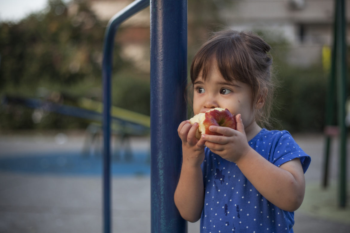 Ein kleines Mädchen isst einen Apfel auf einem Spielplatz