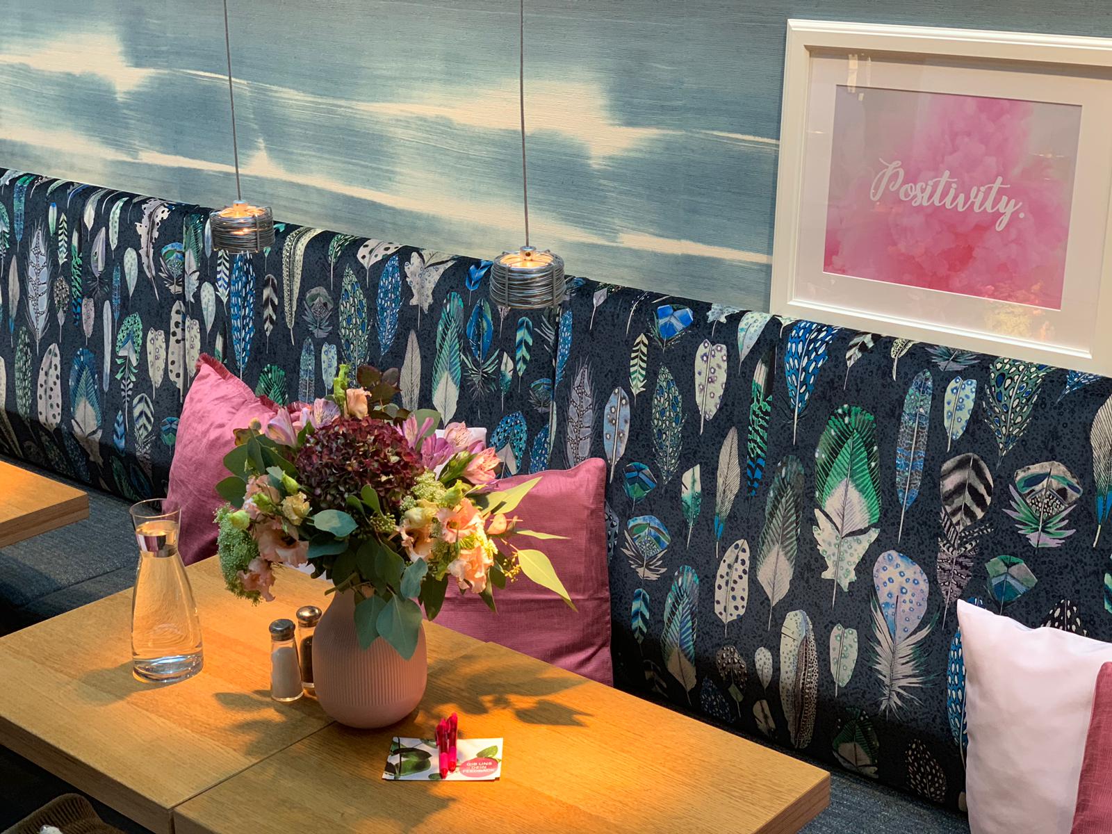 Eine Café-Lounge mit Blumen, Kissen und Bildern.