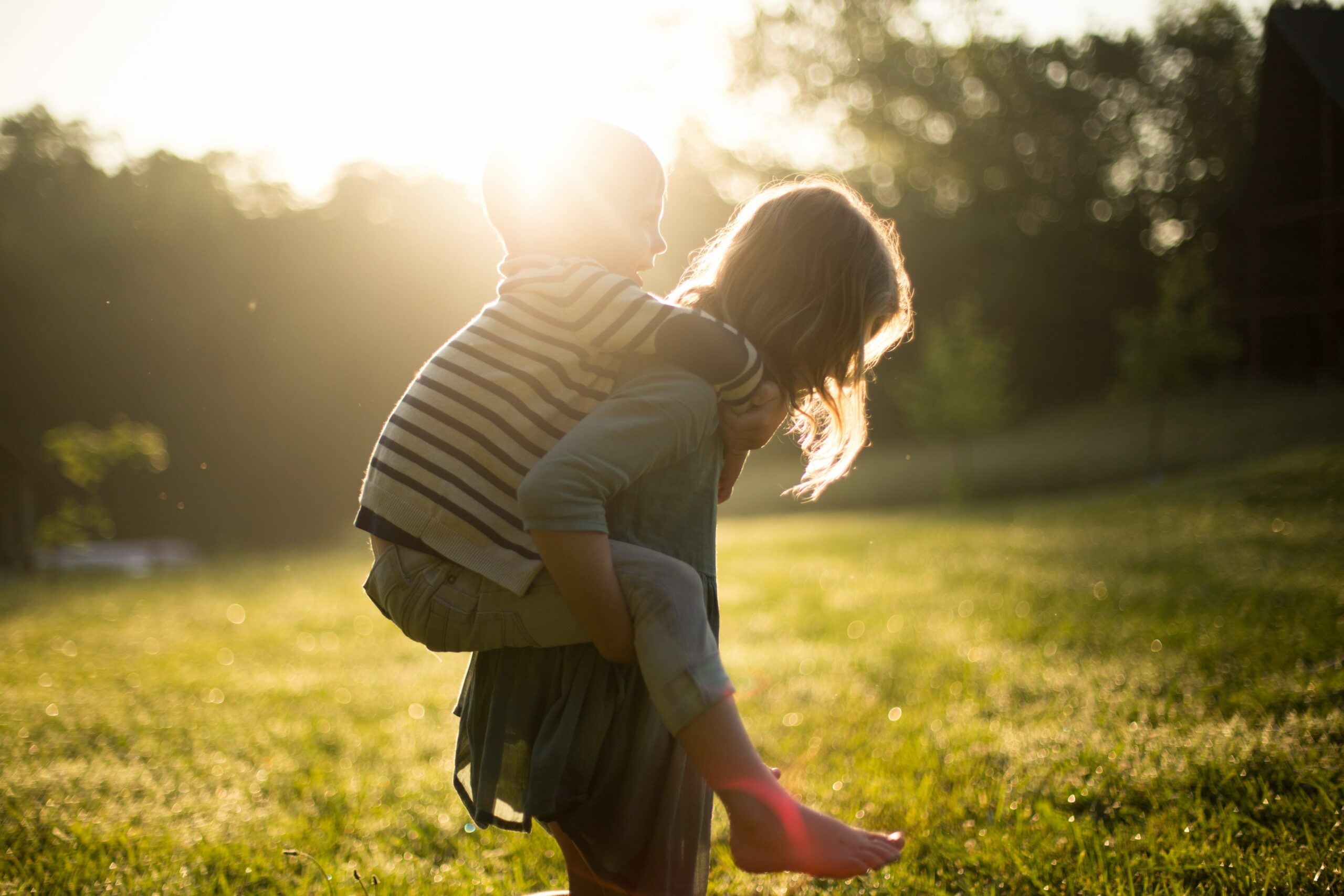 Vitamin D Immunsystem: Mädchen trägt jungen auf dem Rücken auf Rasen mit Sonne.