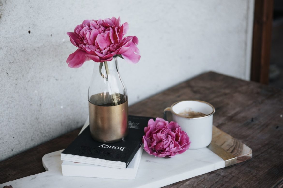 Blume in Vase auf Buch auf einer Kommode mit Tee vor einer weissen Wand