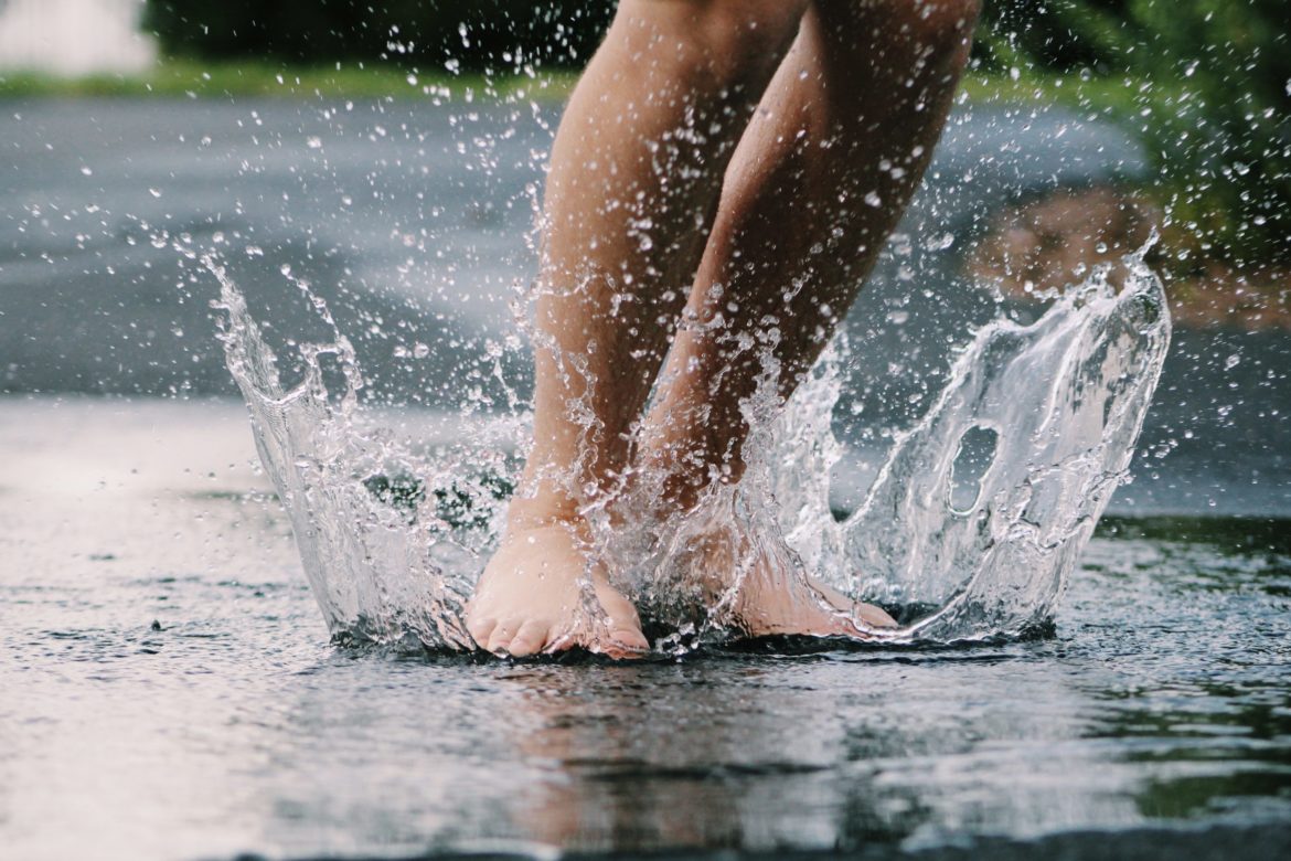 Beine und Füsse in Pfütze bei Regen im Wasser