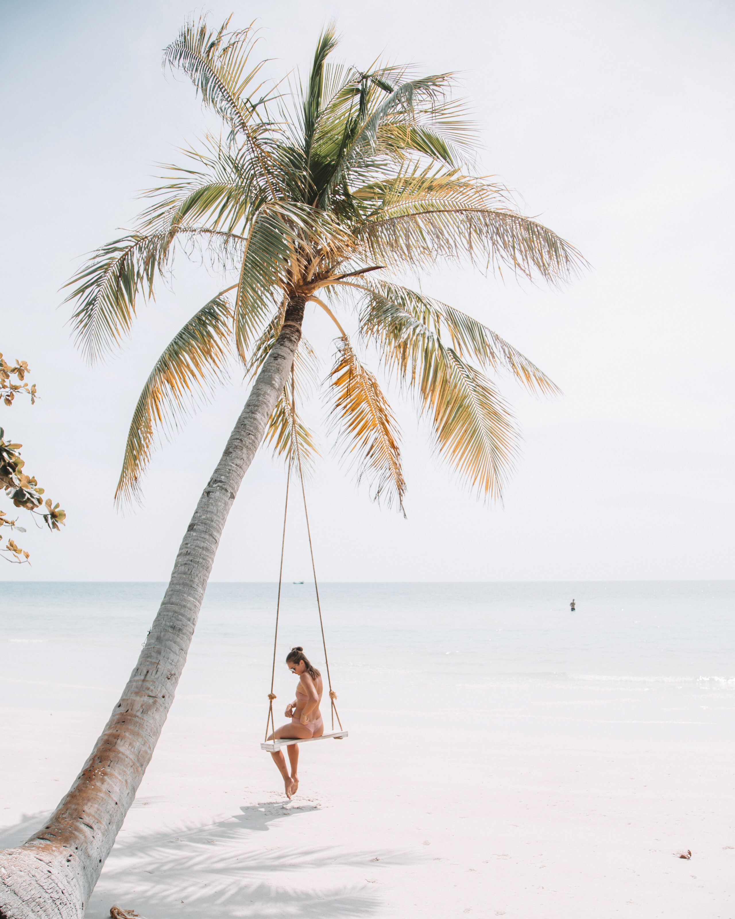 Sonnenschutz Tipps: Frau sitzt auf einer Schaukel unter Palme am Strand