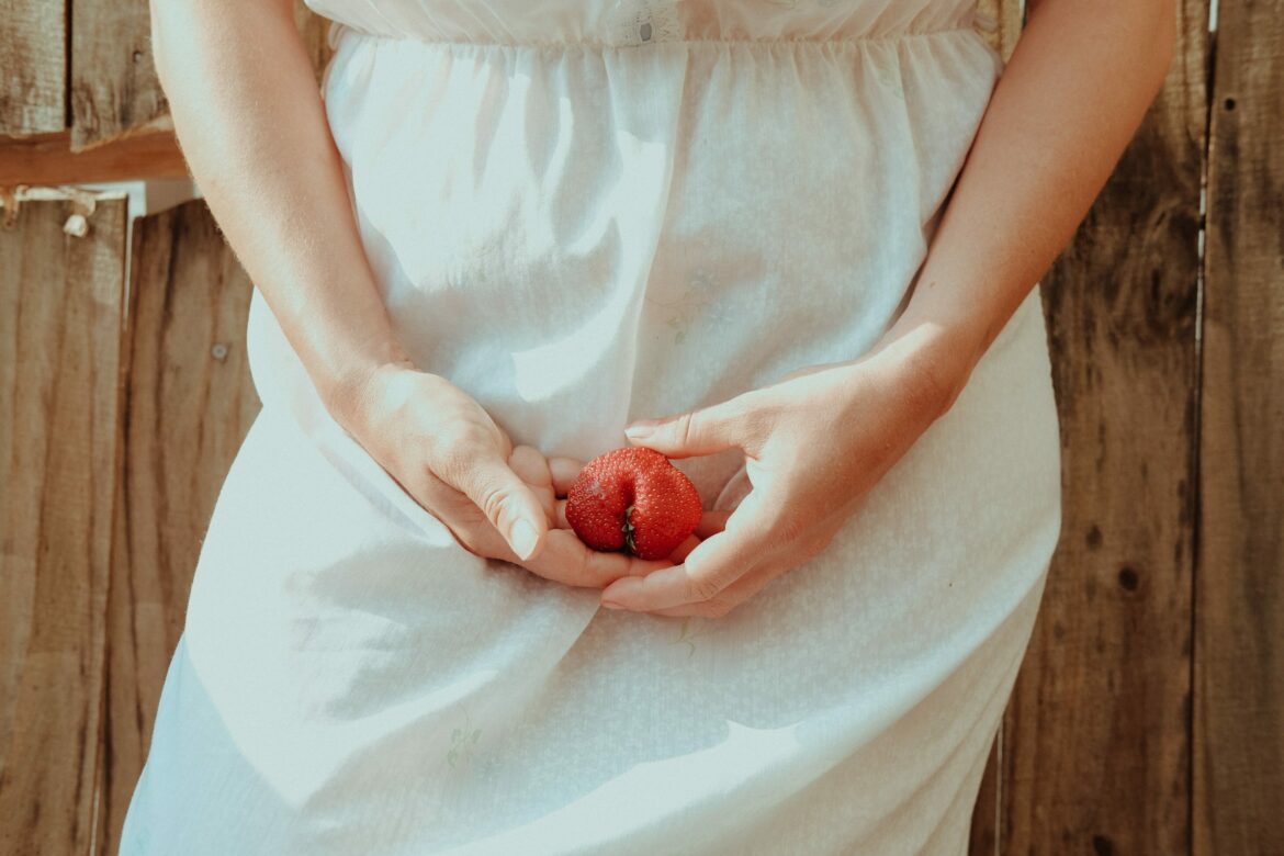 Intimerkrankungen: Frau im weissen Kleid hält sich Erdbeere vor die Körpermitte
