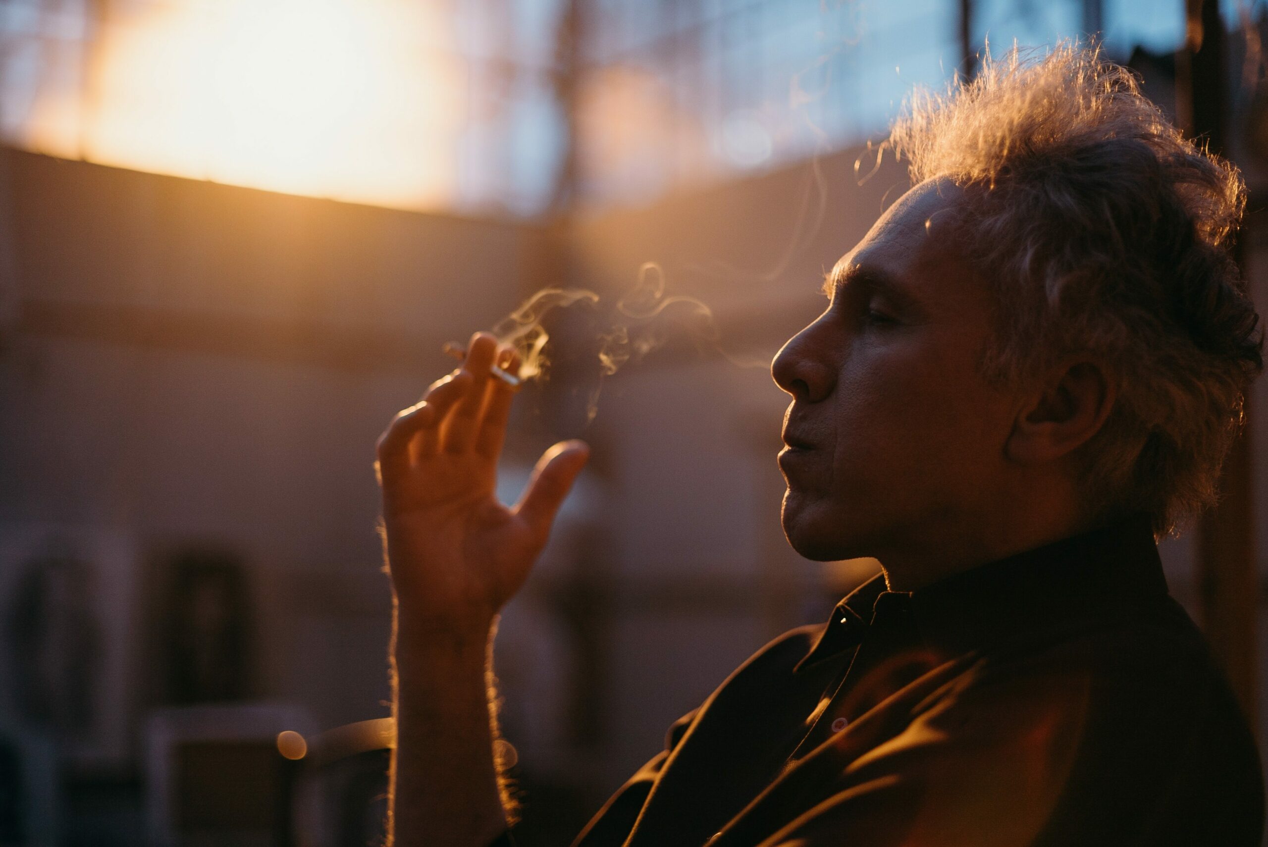 Aufhören zu rauchen: Porträt von einem älteren Mann im Gegenlicht mit Zigarette in der Hand