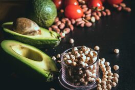 Fettstoffwechsel aktivieren: Komposition aus Erdnüssen, halben Avocados und im Hintergrund Tomaten auf schwarzem Untergrund