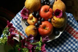 Rheuma Ernährung: Blumenvase und Schale mit Äpfeln, Birnen und Weintrauben auf blau-kariertem Tuch.