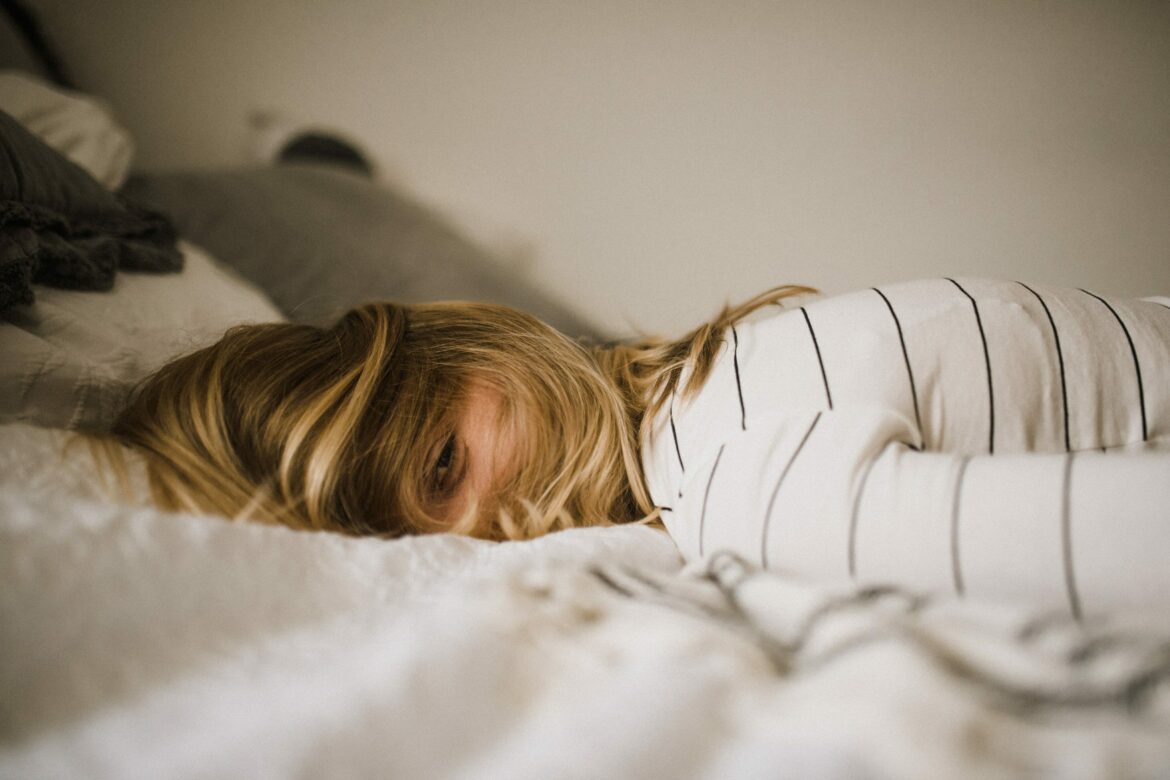 Bauchschmerzen Ursachen: Frau liegt mit dem Gesicht nach unten auf dem Bett