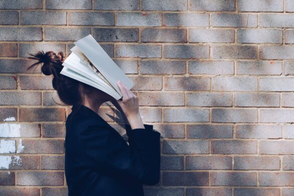Prüfungsangst Schüler: Mädchen hält sich vor einer Mauer ein Buch vors Gesicht