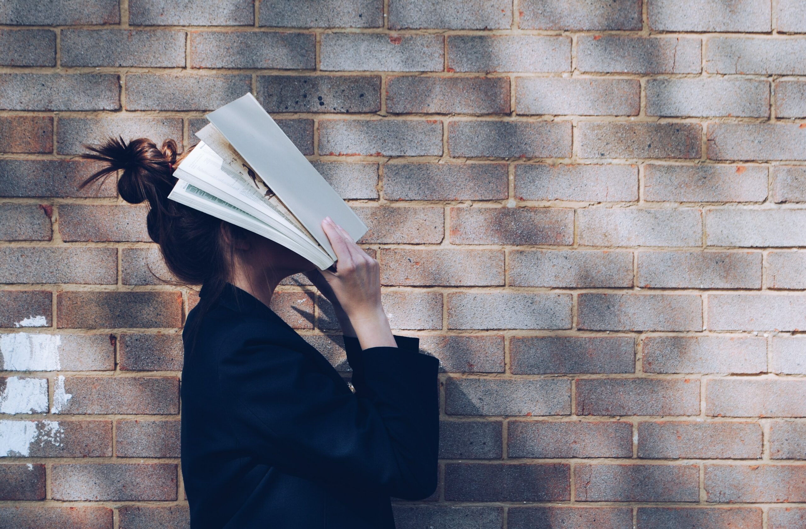 Prüfungsangst Schüler: Mädchen hält sich vor einer Mauer ein Buch vors Gesicht