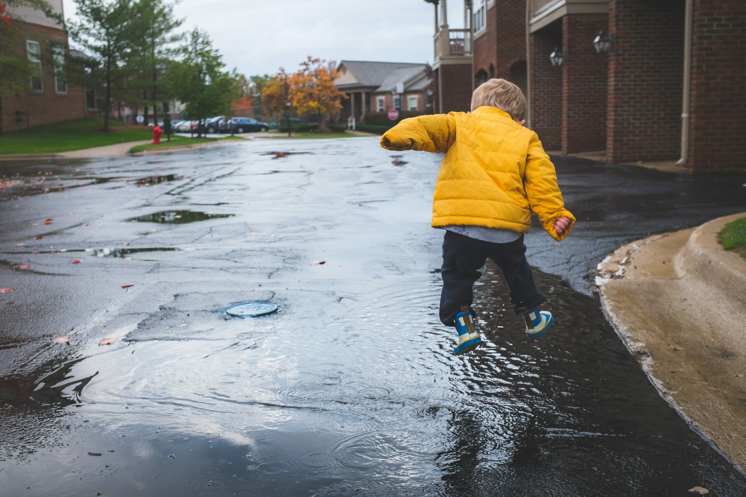 Draussen spielen: Kind mit gelber Regenjacke springt in eine Pfütze.