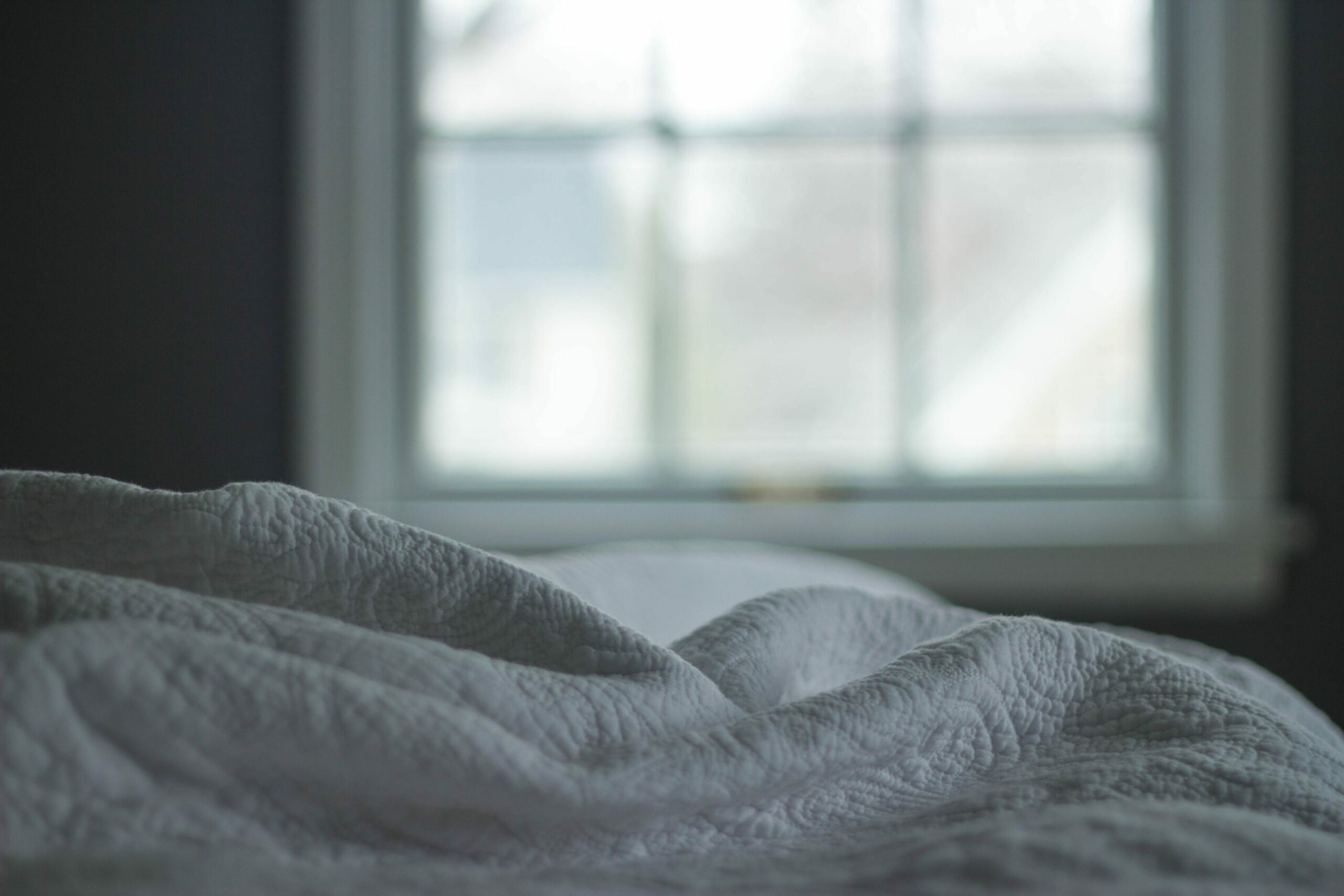 Melatonin Schlafmittel: Weisse Bettdecke und Fenster im Hintergrund.