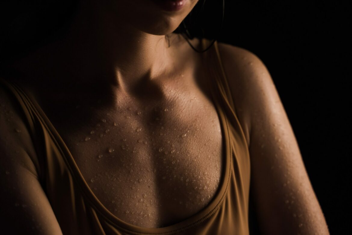 Extremes schwitzen: Nass geschwitztes Dekolleté vor dunklem Hintergrund