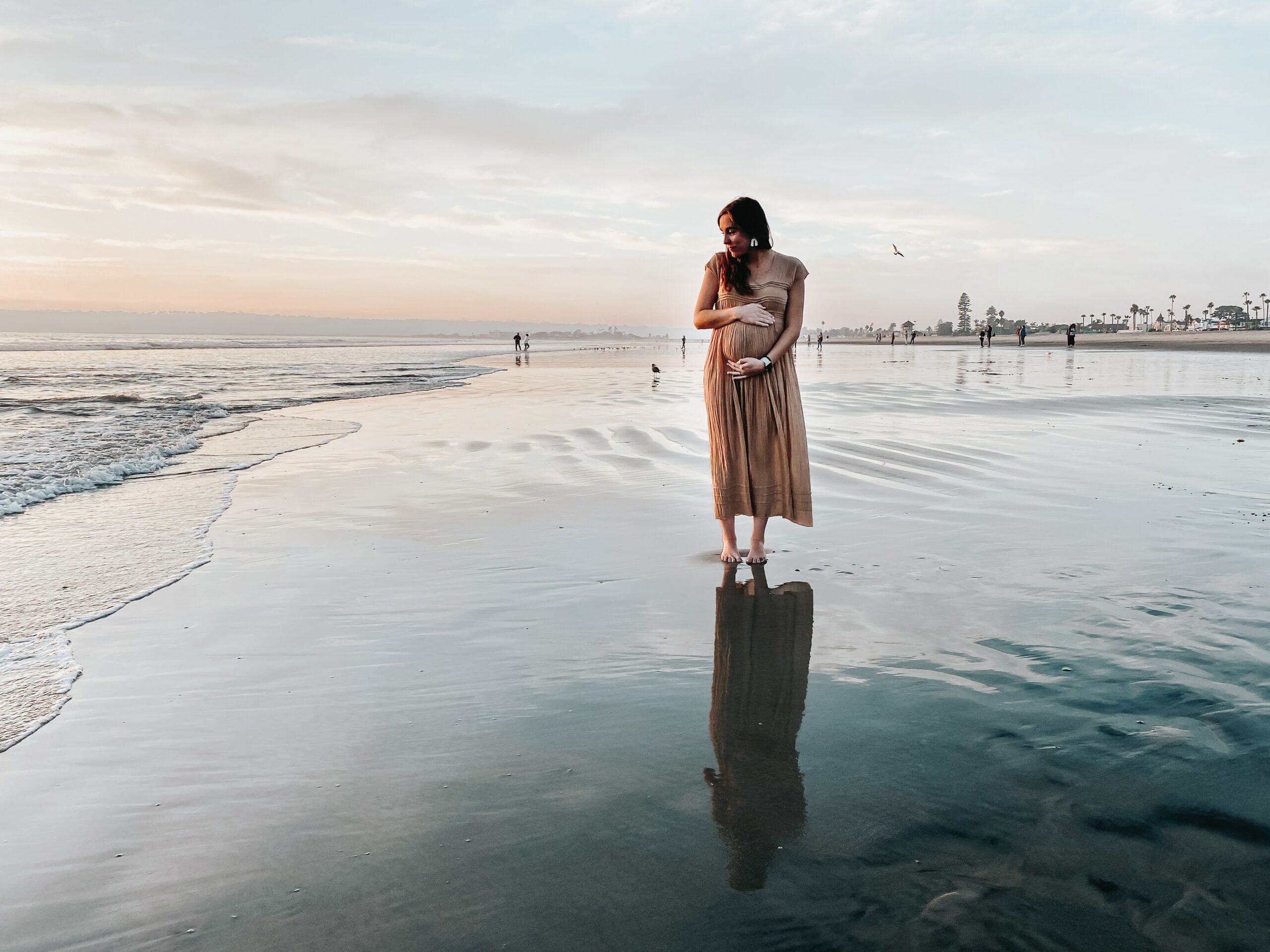 Kindheitstrauma Folgen: Schwangere Frau steht allein am Strand und hält ihren Bauch.