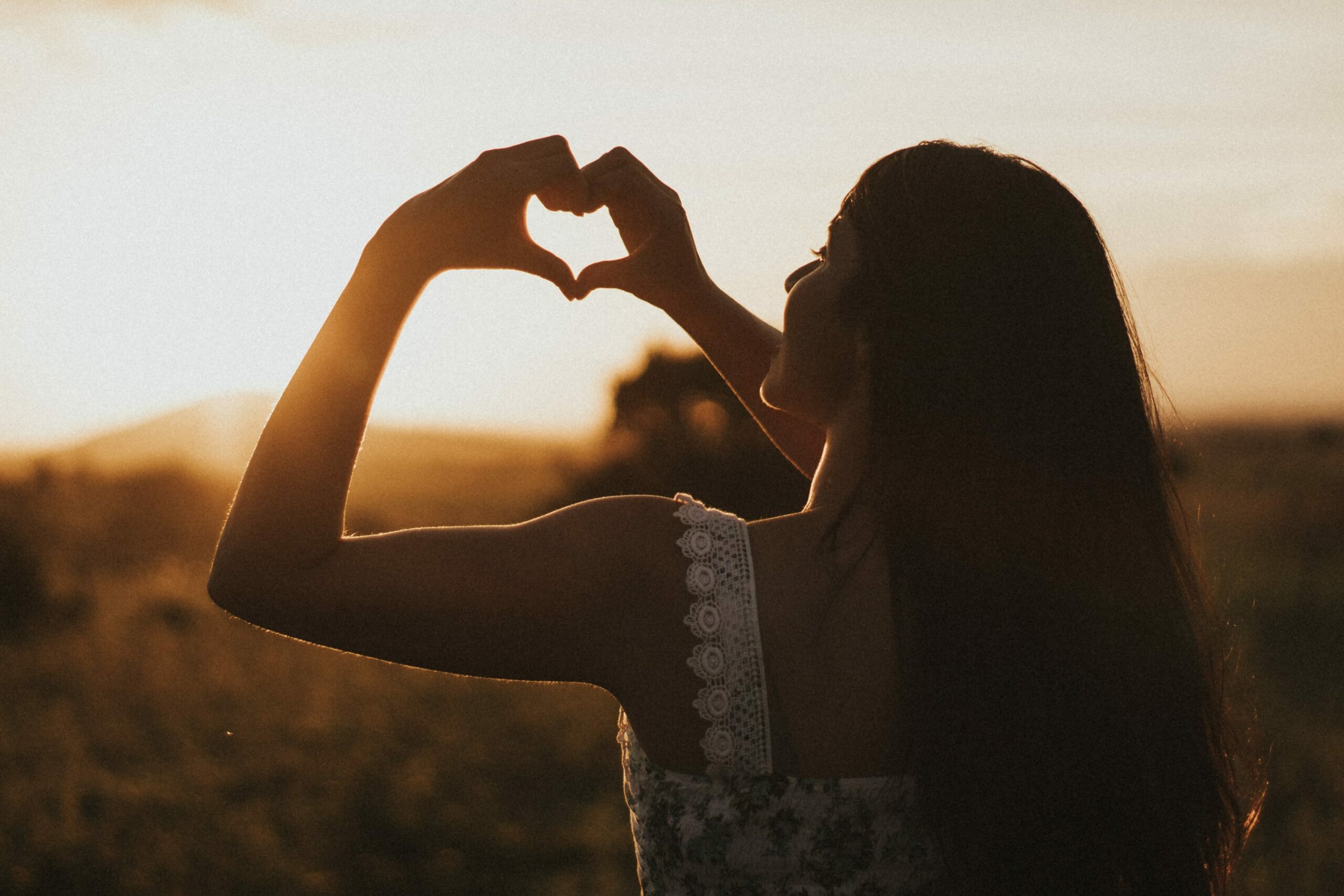 Neurodermitis lindern: Frau formt bei Sonnenuntergang mit ihren Händen ein Herz