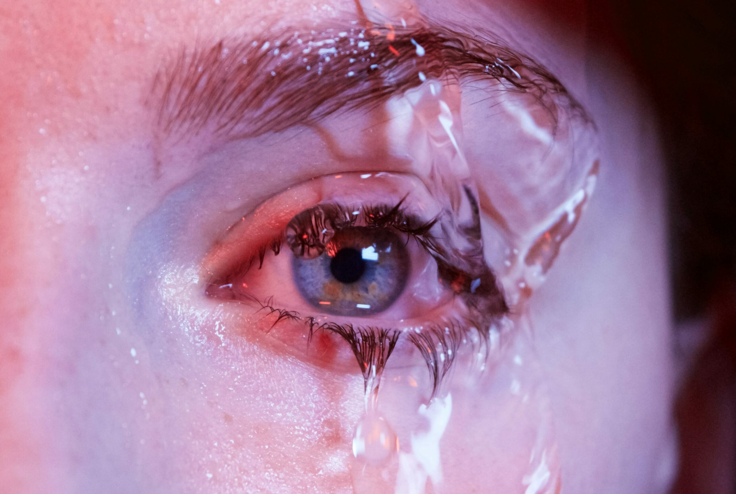Hausmittel Bindehautentzündung: Auge in violettem Licht über das Wasser rinnt