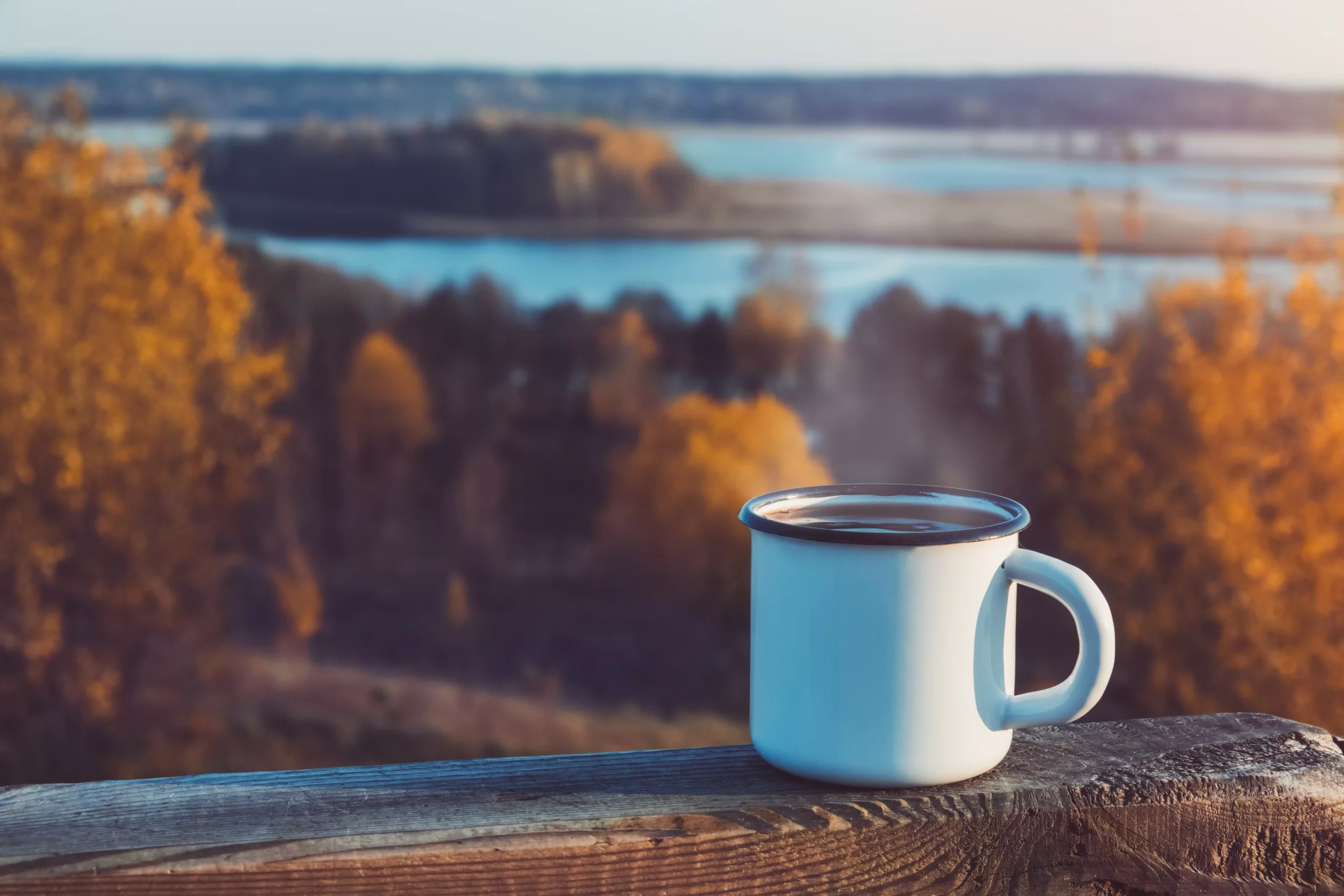 Kaffee nachhaltig: eine Tasse Kaffee steht auf einem Geländer vor einer Herbstlandschaft.