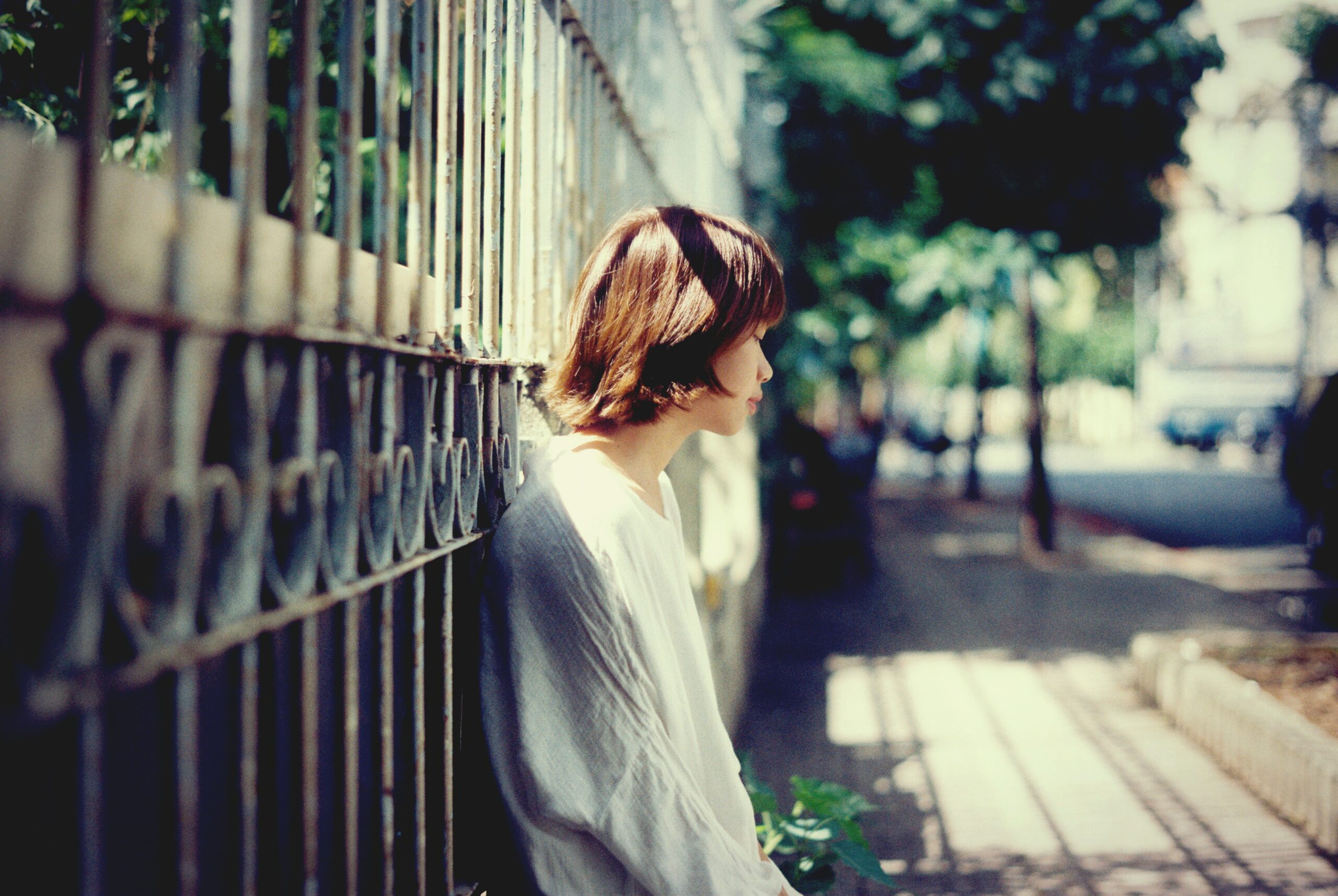 Jugendliche Suizid: Ein trauriges Mädchen lehnt sich mit dem Rücken an einen Zaun.