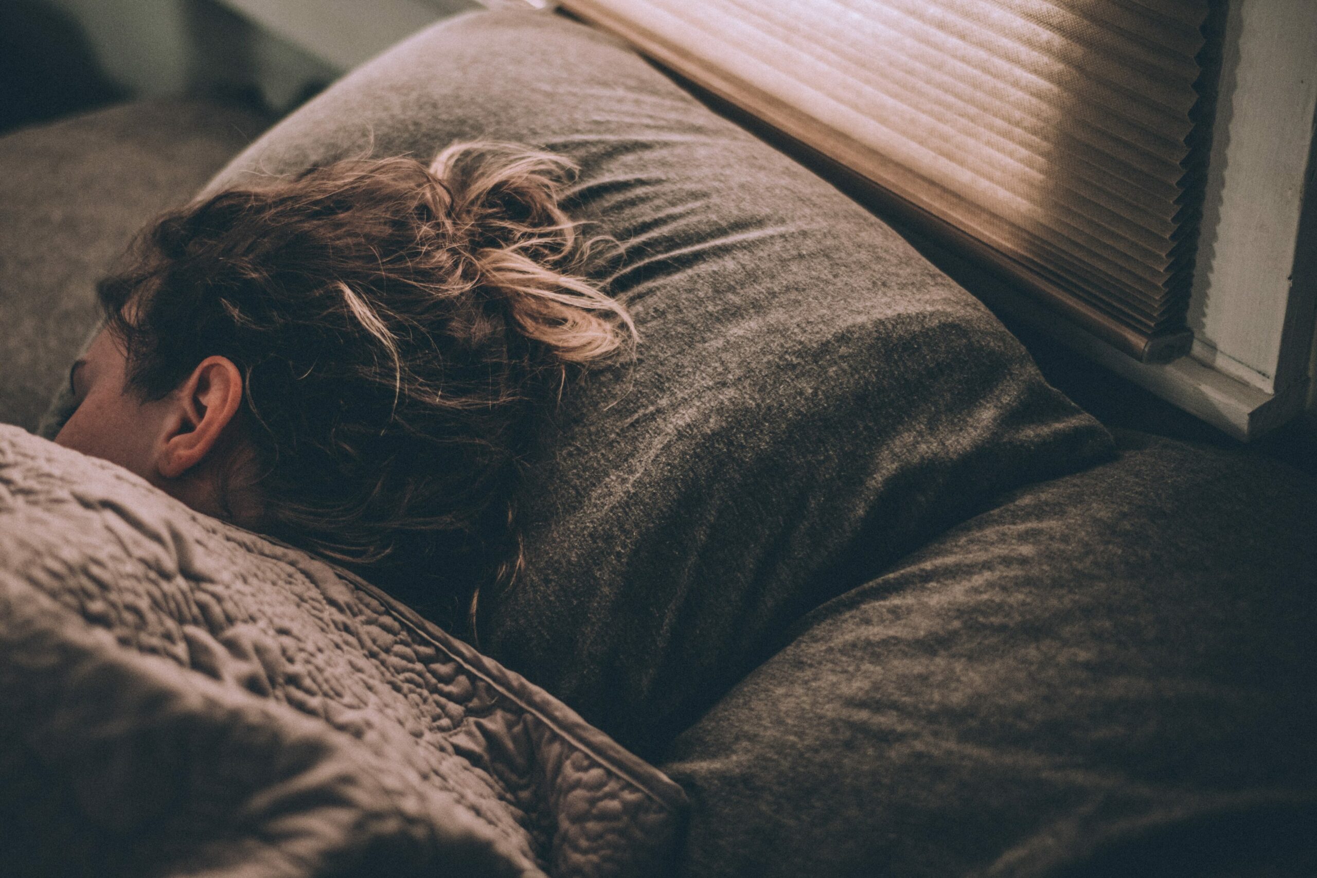 Gehirn im Schlaf: Frau schläft auf der Seite im Halbdunkel und grauer Bettwäsche