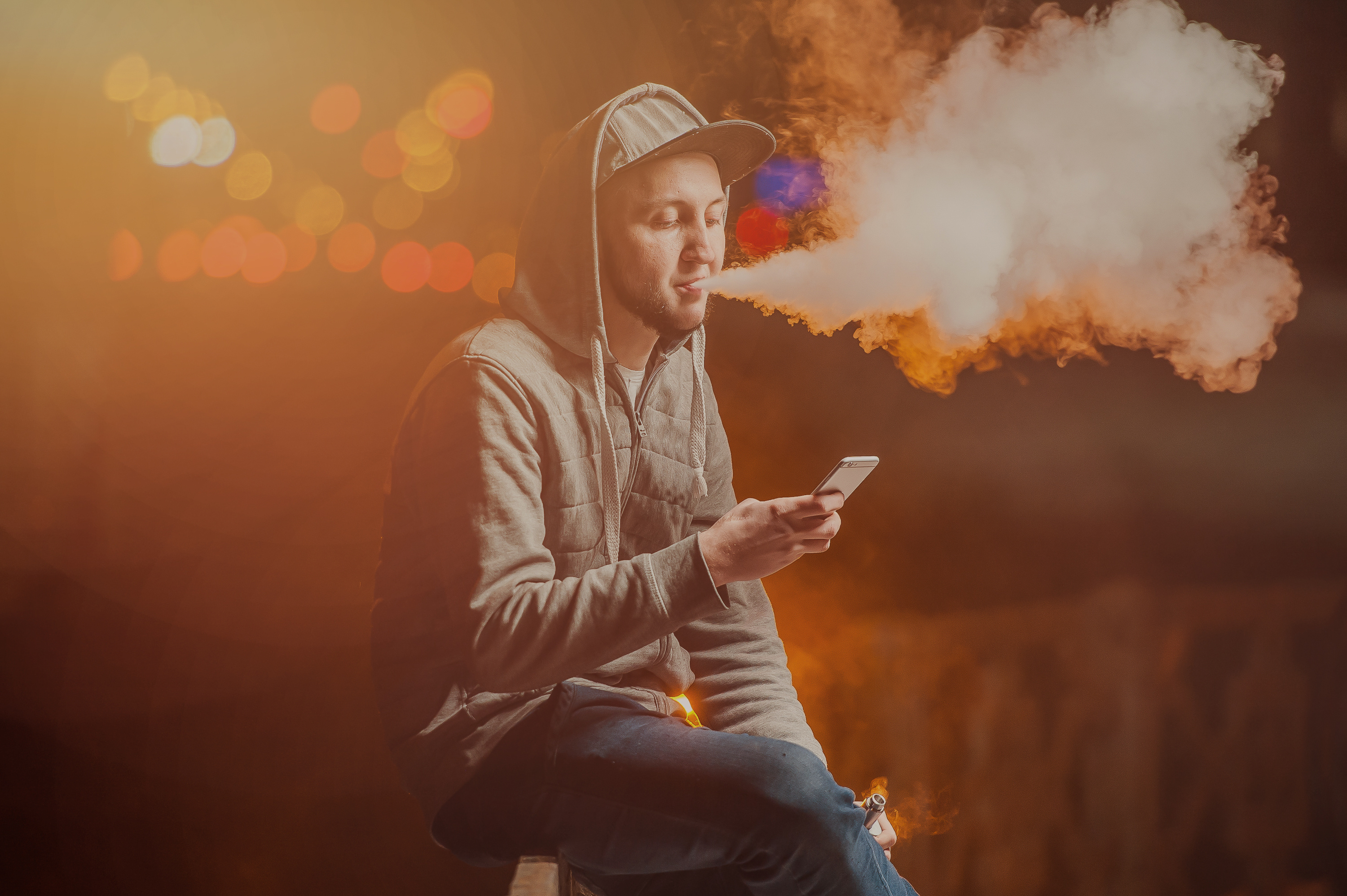 Vaping: junger Mann sitzt im Freien und raucht eine E-Zigarette