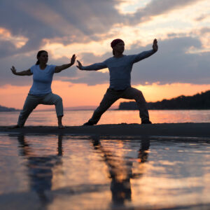 Tai-Chi Parkinson_ Mann und Frau machen Tai-Chi bei Sonnenuntergang am Meer