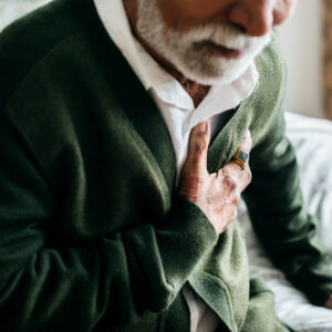 Erste Hilfe Herzinfarkt: Ein älterer Mann greift sich im Sitzen an die Brust.