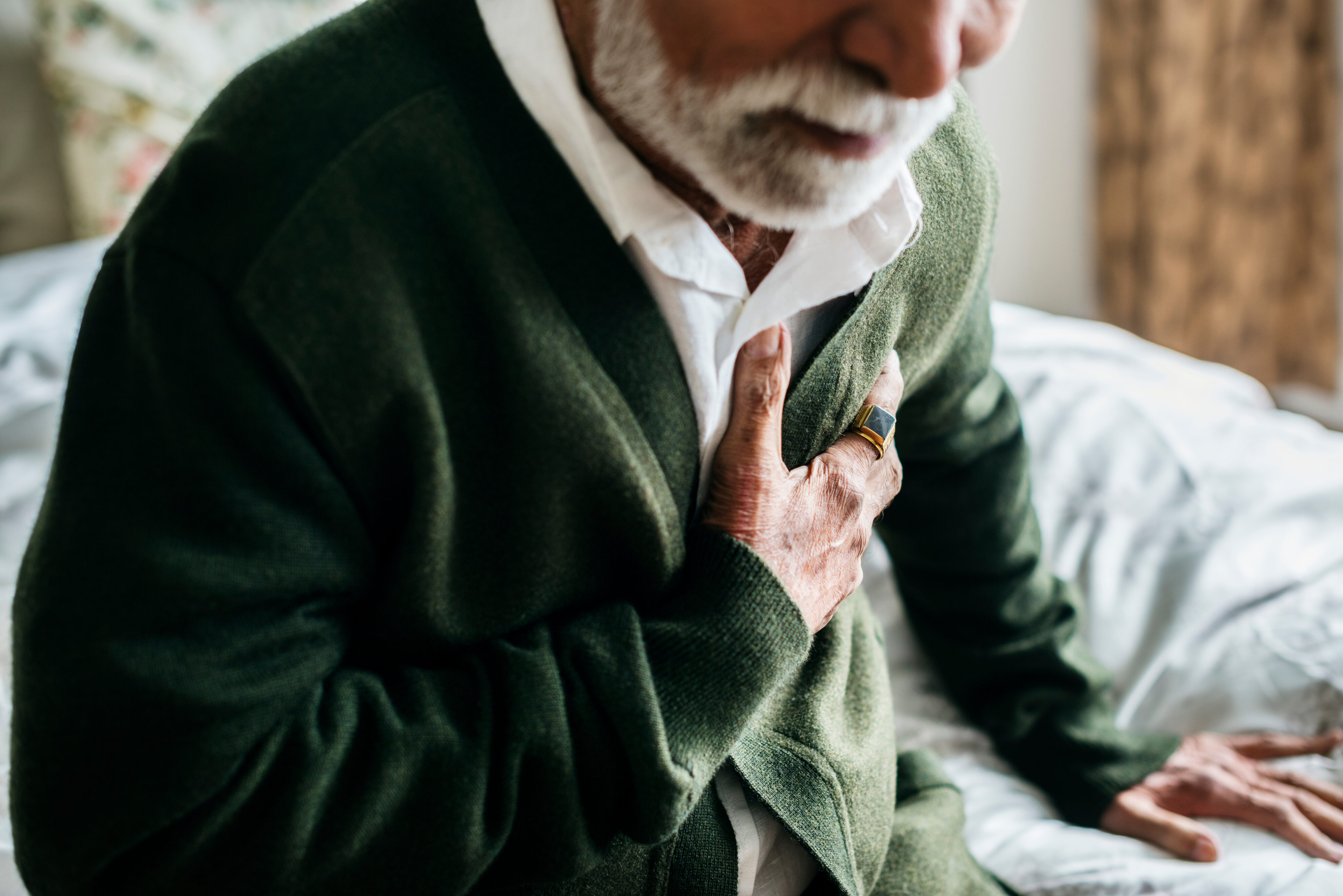 Erste Hilfe Herzinfarkt: Ein älterer Mann greift sich im Sitzen an die Brust.