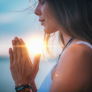 Hormonyoga: Frau meditiert mit aneinanderliegenden Händen und geschlossenen Augen