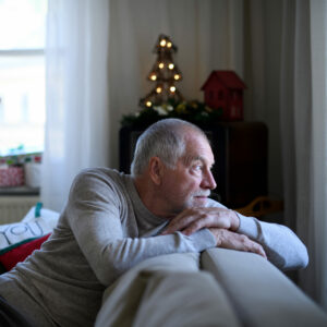Kognitiver Verfall: Älterer Mann sitzt auf dem Sofa und blickt aus dem Fenster.