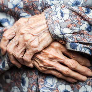 Altern stoppen: vor dem Kleid gefaltete Hände einer sehr alten Frau.