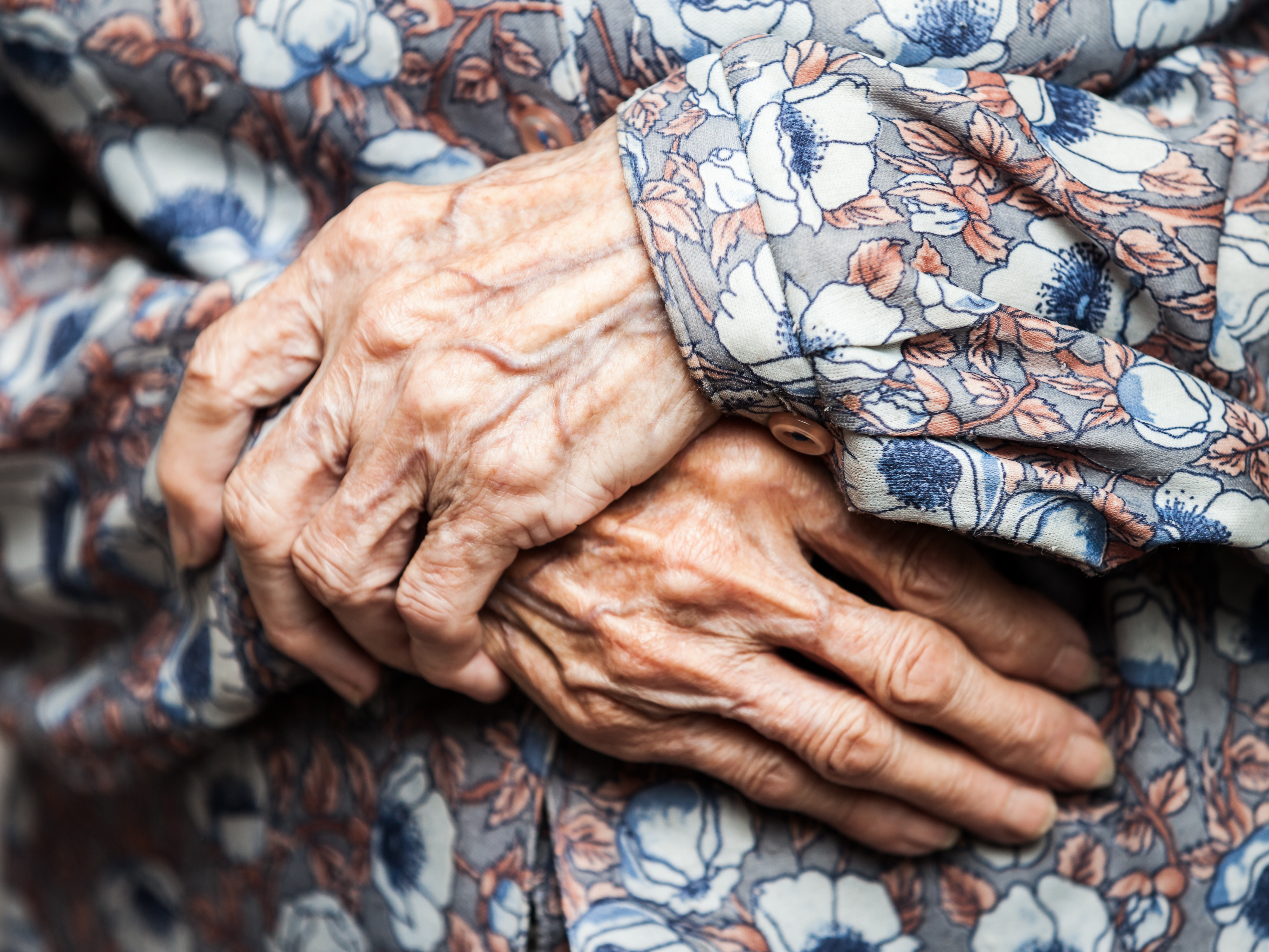 Altern stoppen: vor dem Kleid gefaltete Hände einer sehr alten Frau.