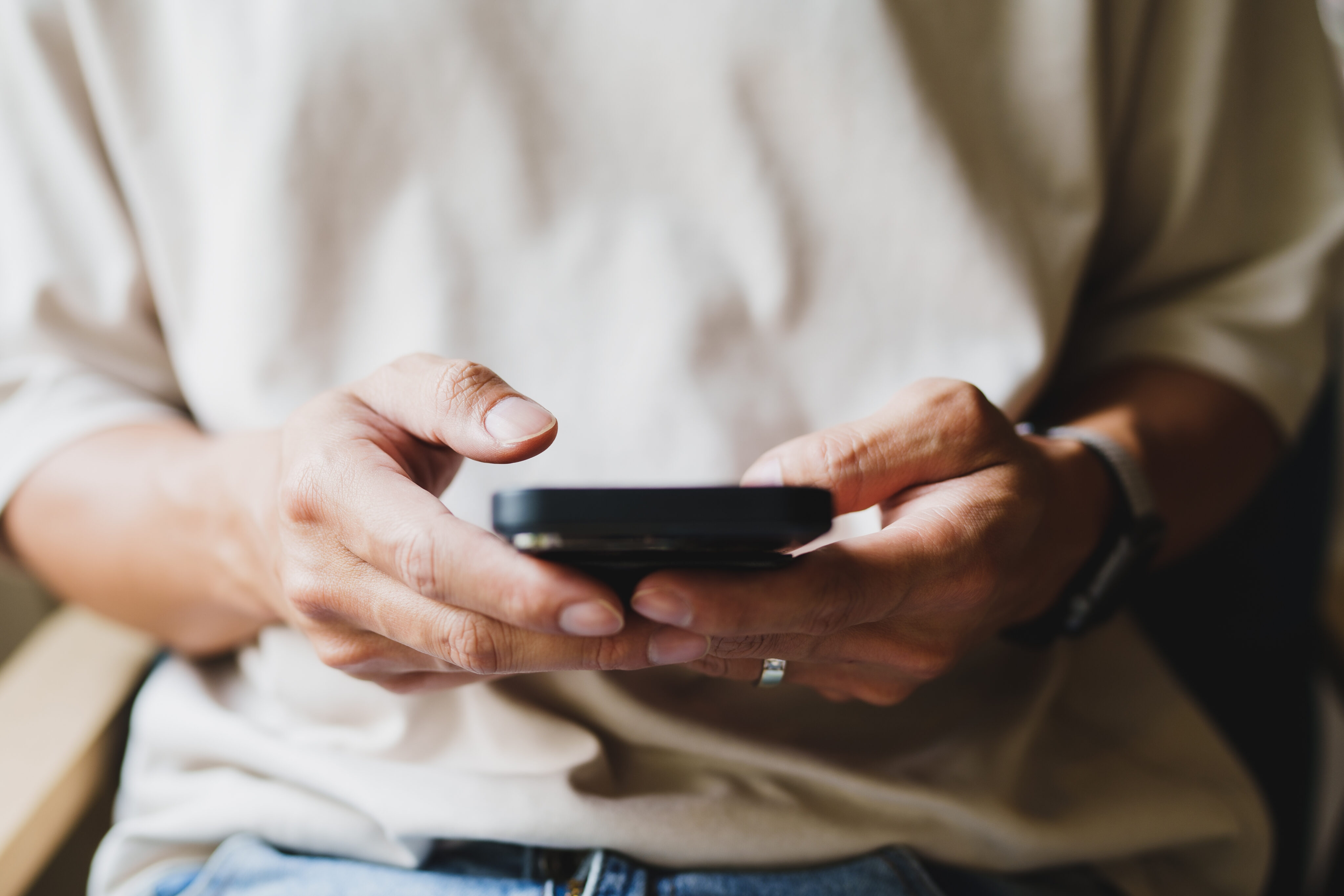 Spermienqualität Handynutzung: Mann hält Mobiltelefon im Sitzen vor sich in der Hand