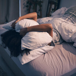 Schlaf messen: Frau liegt im Bett und bedeckt ihr Gesicht mit einem Kissen