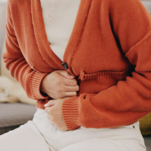 Ursachen für Blähbauch_Stomach ache, cramps and hands of woman with abdomen pain due to constipation, menstruation or ibs issue. Sick, home and person suffering and holding belly in a house lounge, couch and living room.