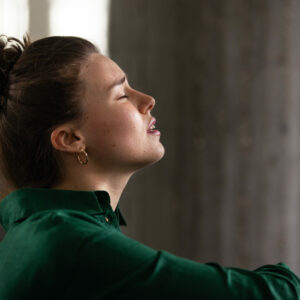 Chronische Schmerzen lindern: Frau sitzt mit schmerzverzerrtem Gesicht an eine Wand gelehnt.