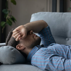 Migräne und Spannungskopfschmerzen: Mann liegt auf der Couch, den Arm über den Augen