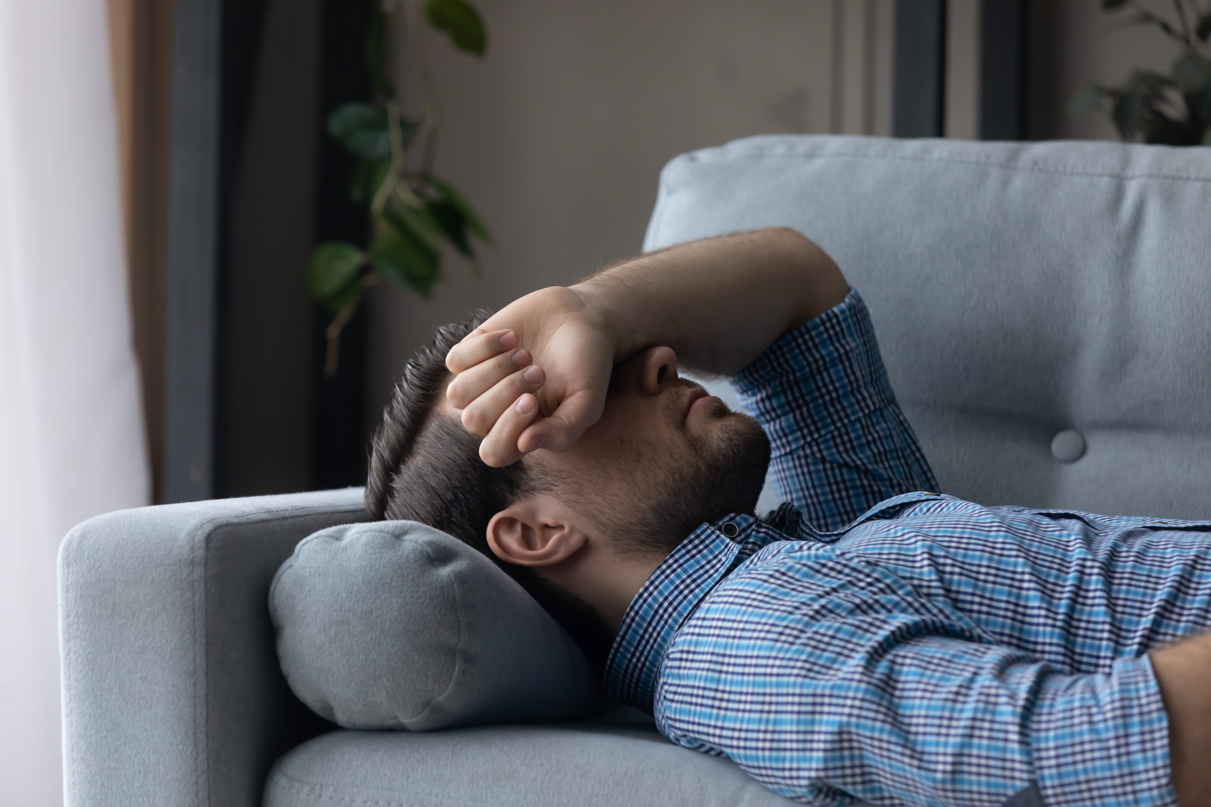 Migräne und Spannungskopfschmerzen: Mann liegt auf der Couch, den Arm über den Augen