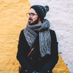 Vorsorgeuntersuchungen bei Männern: Mann in Schal und Mütze und Brille steht vor einer gelben Wand