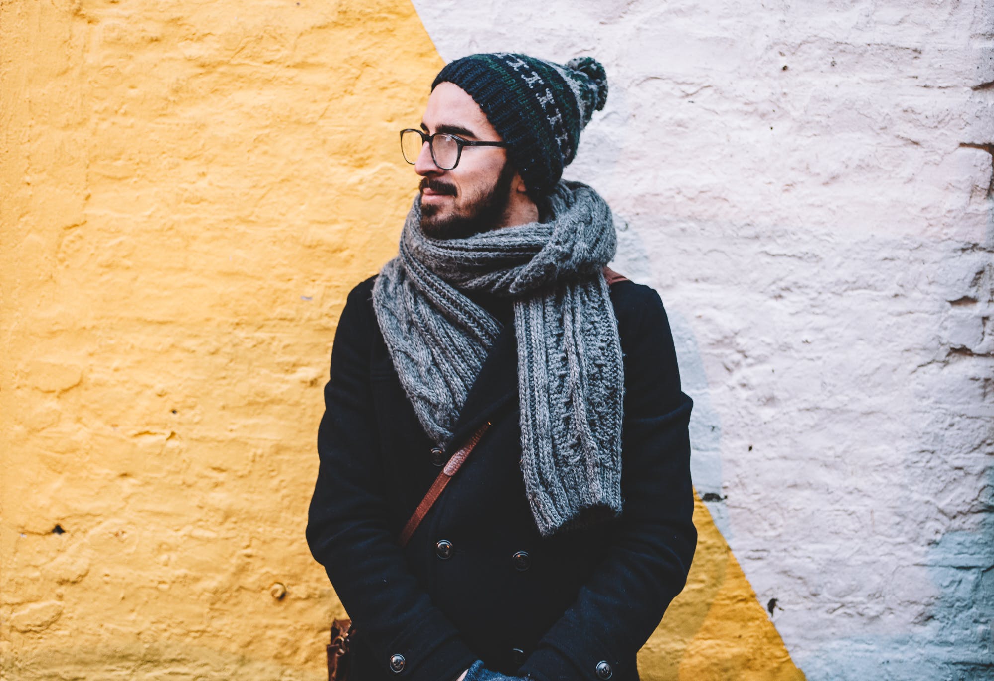 Vorsorgeuntersuchungen bei Männern: Mann in Schal und Mütze und Brille steht vor einer gelben Wand