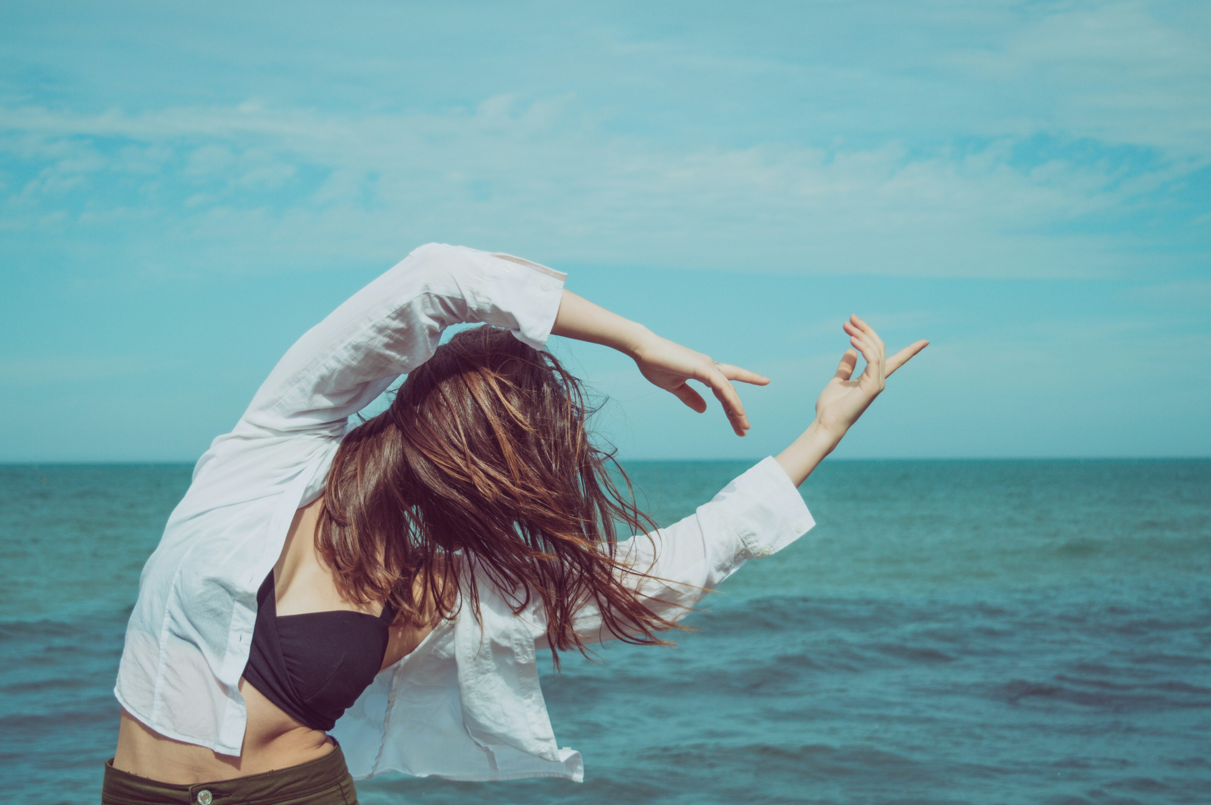 Tanzen Übergewicht: Frau in Bewegung am Strand, gestikuliert tanzend mit ausgestreckten Armen gegen den Hintergrund des Meeres, ein inspirierendes Bild, das den positiven Einfluss von Tanzen auf die körperliche Aktivität und das Gewichtsmanagement hervorhebt.