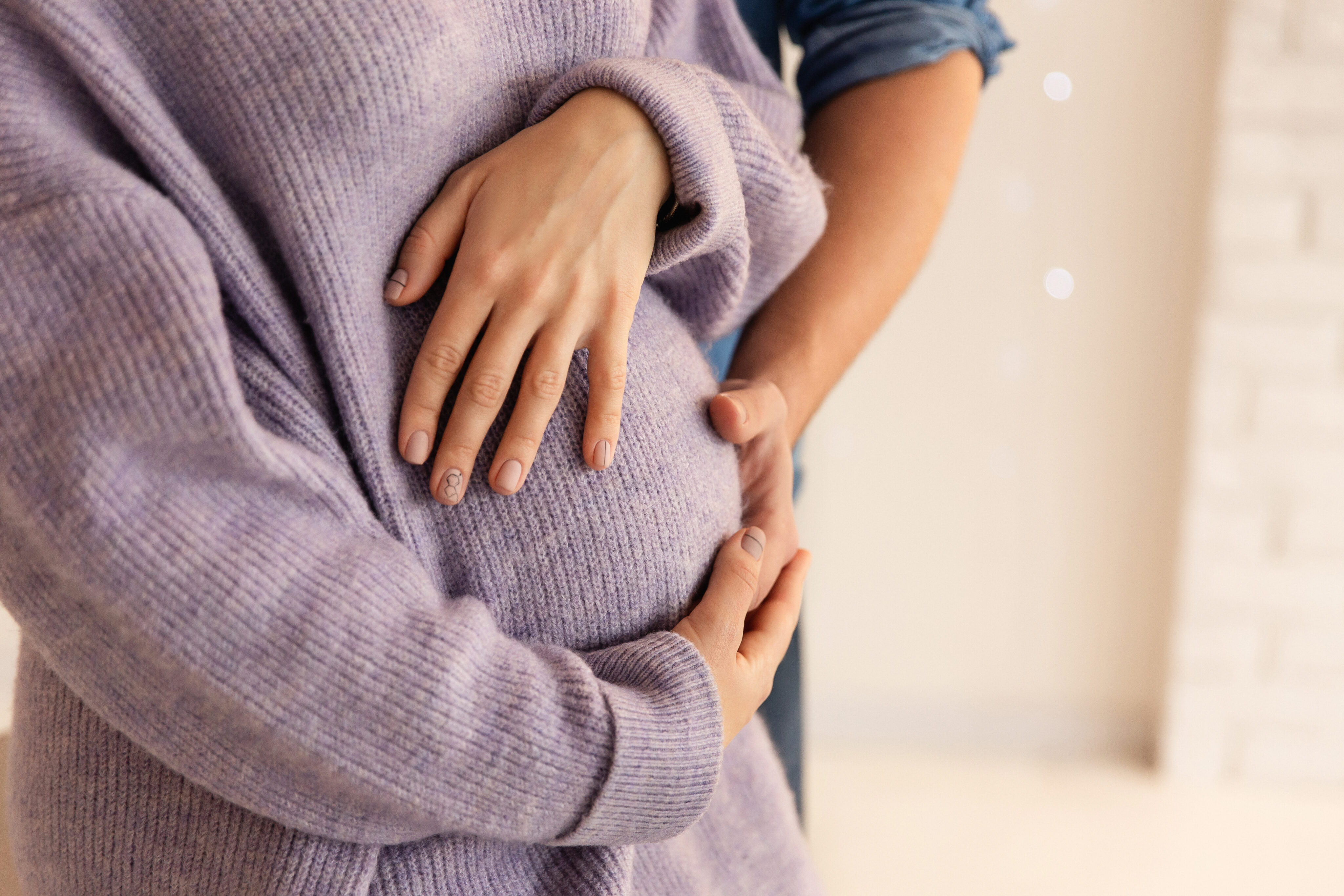 Schwangerschaft Alter: Paar umfasst Babybauch mit beiden Händen.